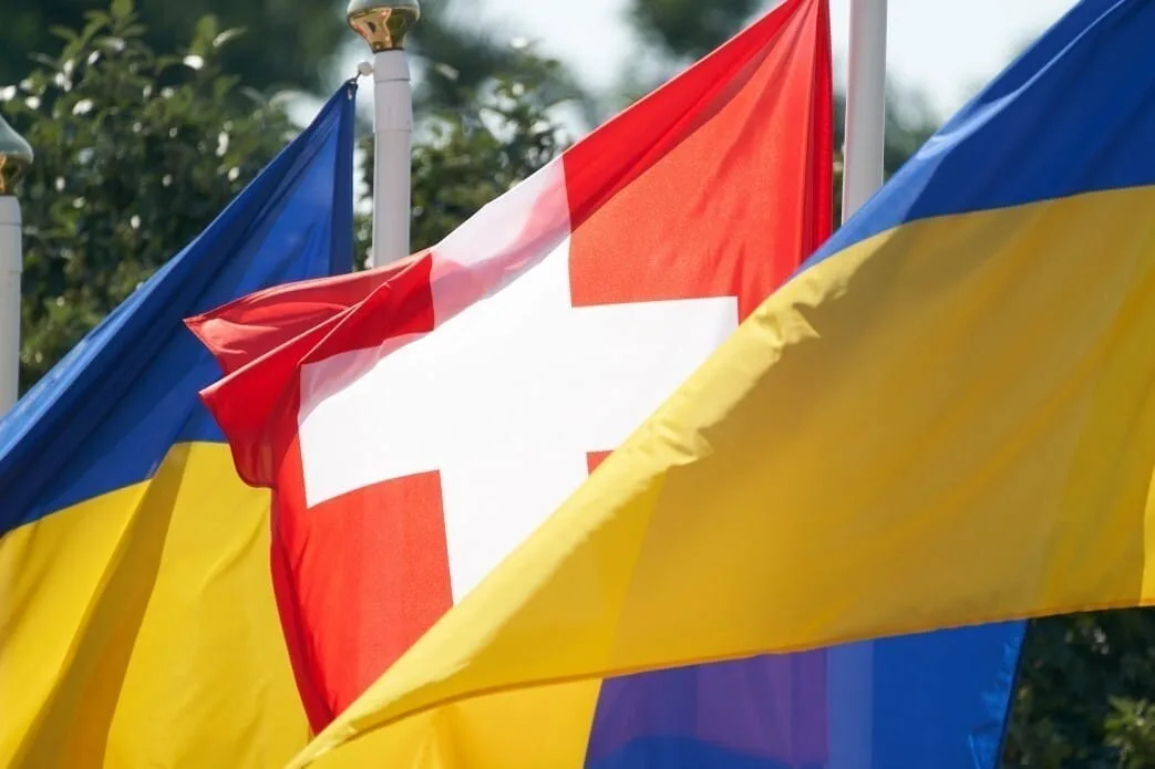 Прапори України та Швейцарії на тлі інфраструктурного обʼєкта